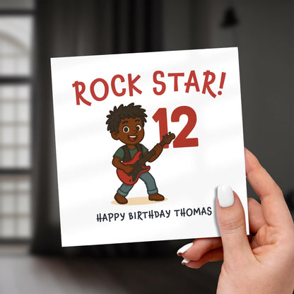 Hand holding a birthday card with a rock star design and text 'Rock Star! 12 Happy Birthday Thomas'.