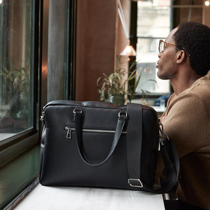 Man sitting at a table with a black leather briefcase in front of him, looking out a window.