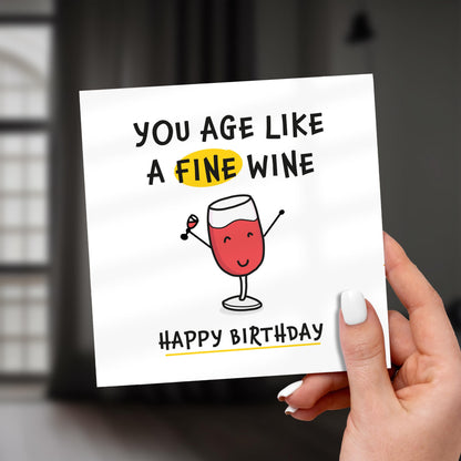 Hand holding a birthday card with a wine glass illustration and humorous text.