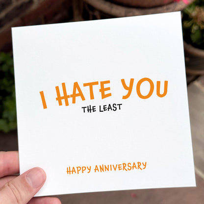 Card with 'I HATE YOU THE LEAST' and 'Happy Anniversary' text held by a hand.