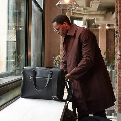 Man in a brown coat standing next to a black briefcase in an indoor setting.