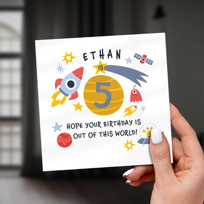 Hand holding a birthday card with space-themed design and text.