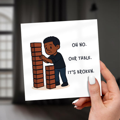 Hand holding a card with a cartoon illustration of a child building a table with blocks and text 'Oh no, our table. It's broken.