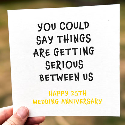 Hand holding a card with humorous 25th wedding anniversary message.