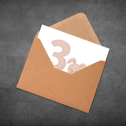 Brown envelope with a white card featuring a pink number '3' and a bunny on a dark gray background