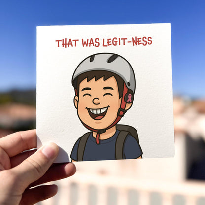 Card with a cartoon character wearing a helmet and text 'THAT WAS LEGIT-NESS' held by a hand against a blurred outdoor background.