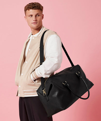 Man holding a black leather bag against a pink background