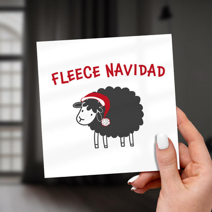 Card with a black sheep wearing a Santa hat and 'Fleece Navidad' text, held by a hand.