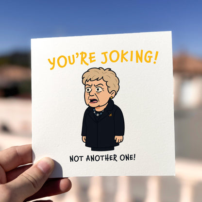 Cartoon character holding a card with text 'YOU'RE JOKING! NOT ANOTHER ONE!' against a blurred outdoor background.