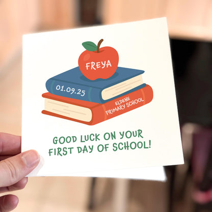 Card with books and an apple illustration, personalized for a first day of school, held by a hand.
