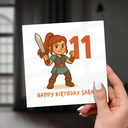 Birthday card with a character holding a sword and the number 11, held by a hand.