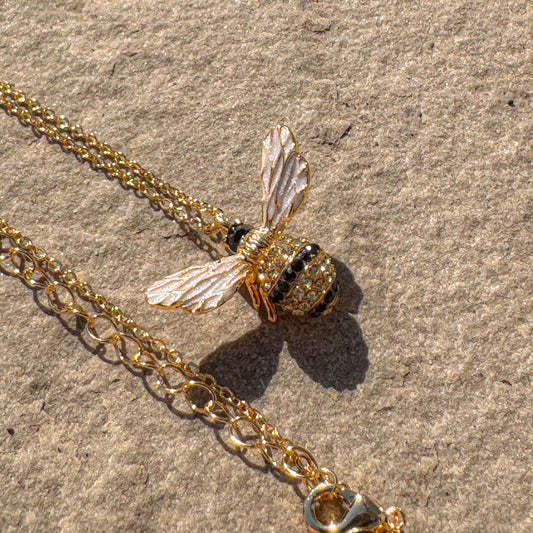Large gold bee pendant necklace with crystal details, shown on stone background with extender chain visible