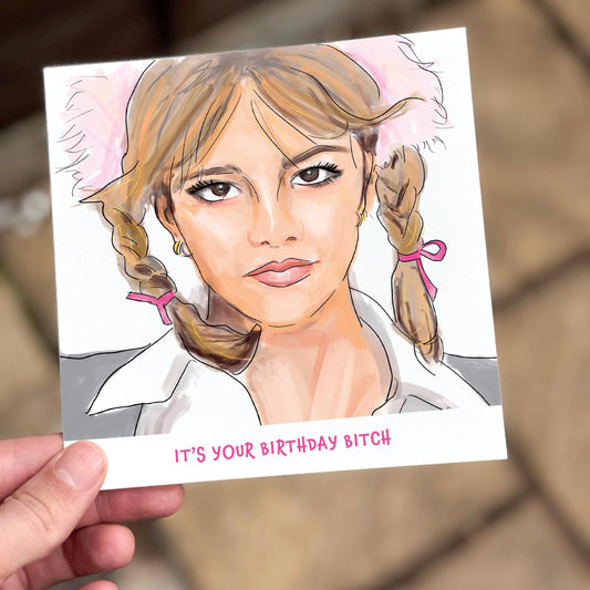A square birthday card held in hand featuring a bold illustration of a pop culture icon with blonde pigtails, pink ribbons, and a fluffy headband. Below reads “It’s Your Birthday Bitch” in playful pink font – a sassy and fun birthday card.