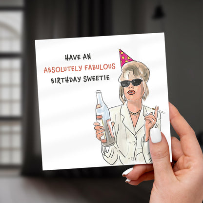 Hand holding a birthday card with a person wearing sunglasses and a party hat, text 'Have an Absolutely Fabulous Birthday Sweetie'.