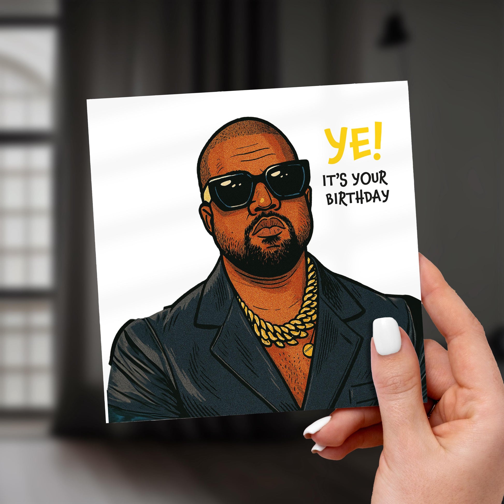 Hand holding a card with a stylized illustration of a person wearing sunglasses and a gold chain, with text 'YE! IT'S YOUR BIRTHDAY'.