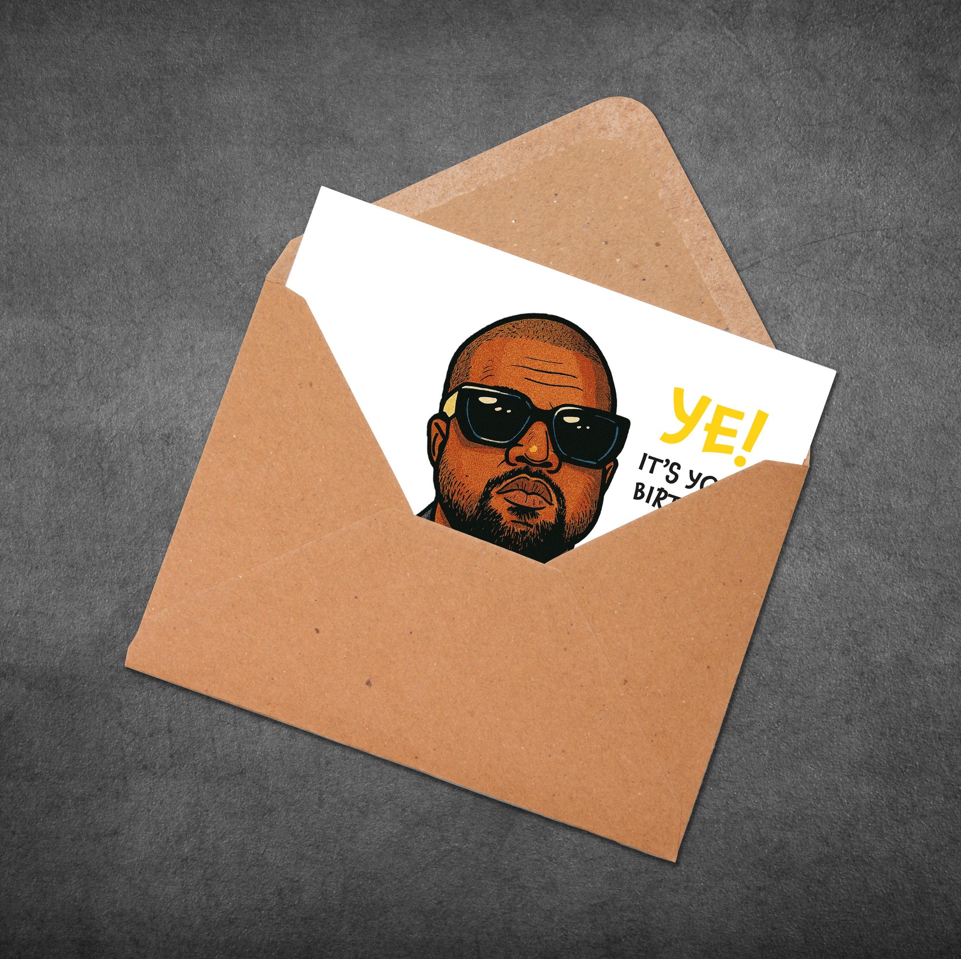 Card with a face design and 'YE! IT'S YOUR BIRTHDAY' text in an open brown envelope on a gray background