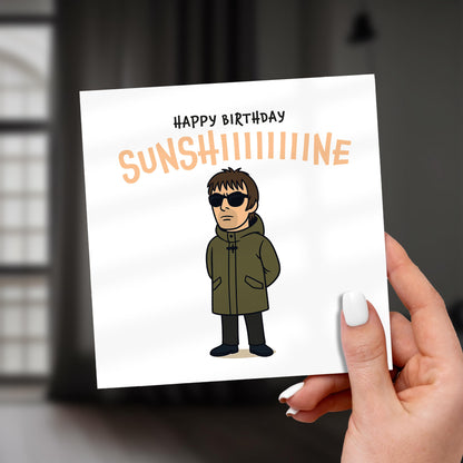 Hand holding a birthday card with a cartoon character and 'Happy Birthday Sunshine' text.