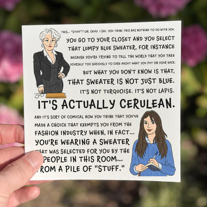 Square illustrated card showing two cartoon women: one in a black pinstripe suit holding glasses, the other in a blue sweater holding a notebook. The card is filled with a long quote from The Devil Wears Prada, ending with the phrase “IT’S ACTUALLY CERULEAN.” White background, dramatic fashion-industry tone.
