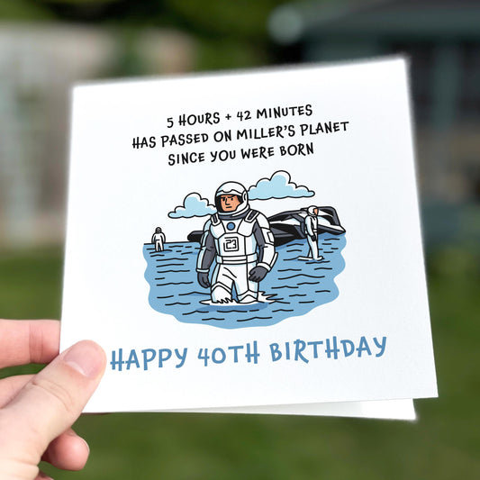 Birthday card with an astronaut illustration and humorous text, held by a hand.