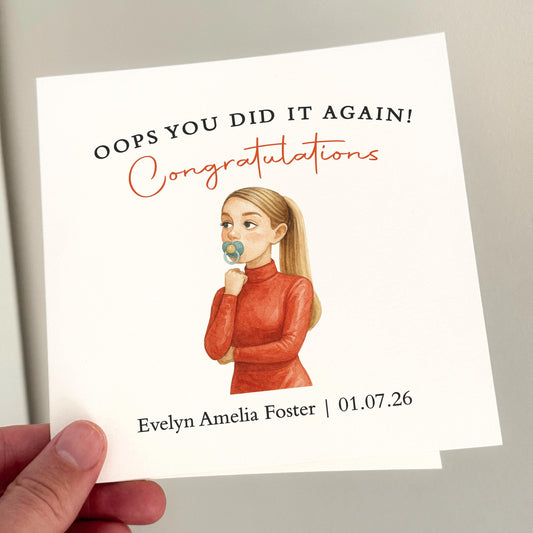 A square white card held in hand featuring a watercolour illustration of a woman with a ponytail sucking a dummy, wearing a red top. Above her reads “Oops You Did It Again! Congratulations” with baby name and date below. A witty and personalised new baby card.