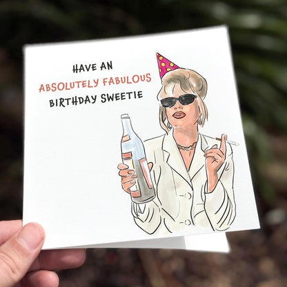 Birthday card with illustration of a woman holding a bottle and text 'Have an Absolutely Fabulous Birthday Sweetie' on a white background.
