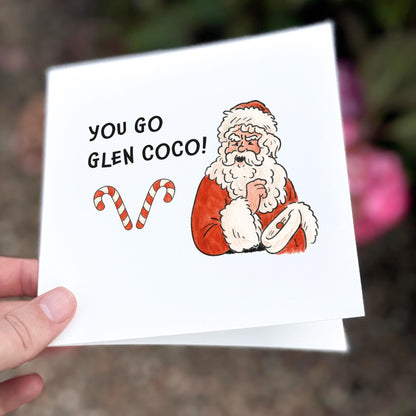 Square illustrated Christmas card featuring a cartoon Santa holding a list, smiling smugly beside two candy canes. Bold black text reads “YOU GO GLEN COCO!” in reference to the iconic Mean Girls quote. Background is white, and the tone is festive, sassy, and pop culture inspired.