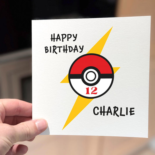 A square birthday card with a bold red and white Pokéball-style design in the centre, featuring the number 12. A bright yellow lightning bolt runs behind it, with "Happy Birthday" and the name "Charlie" in playful, cartoon-style font. The card has a clean white textured background and a fun, energetic mood — ideal for a Pokémon fan.