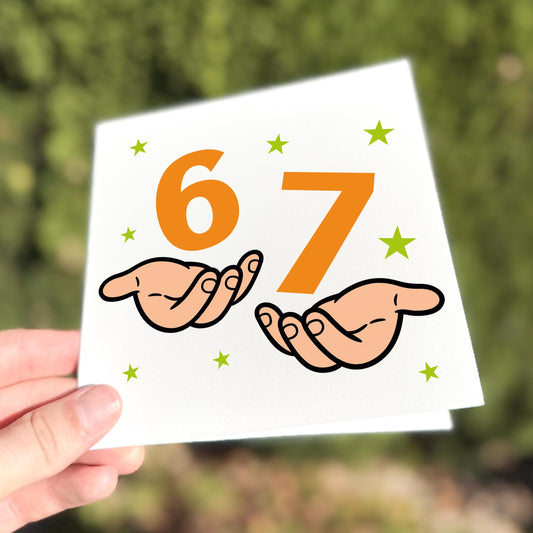 Square greeting card held outdoors in natural light. The card shows the numbers “6” and “7” in bold orange text, each resting on an illustrated open hand, surrounded by small green stars. The design references the Gen Z viral phrase “it’s six seven, not sixty-seven.”